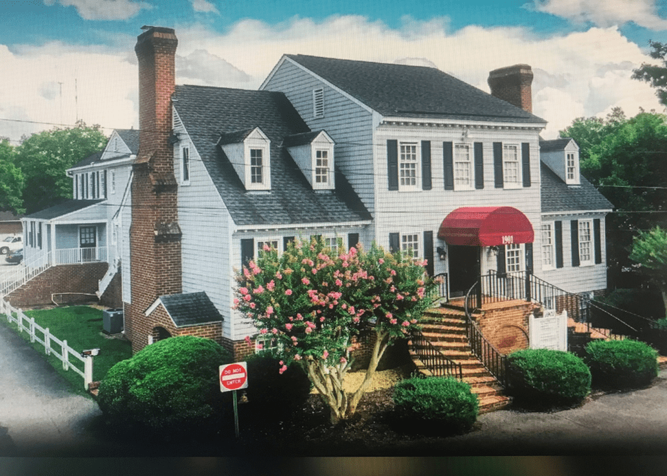 Large white house with a red canopy entrance and flower garden.