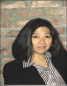 Woman with black hair smiling against a brick wall.